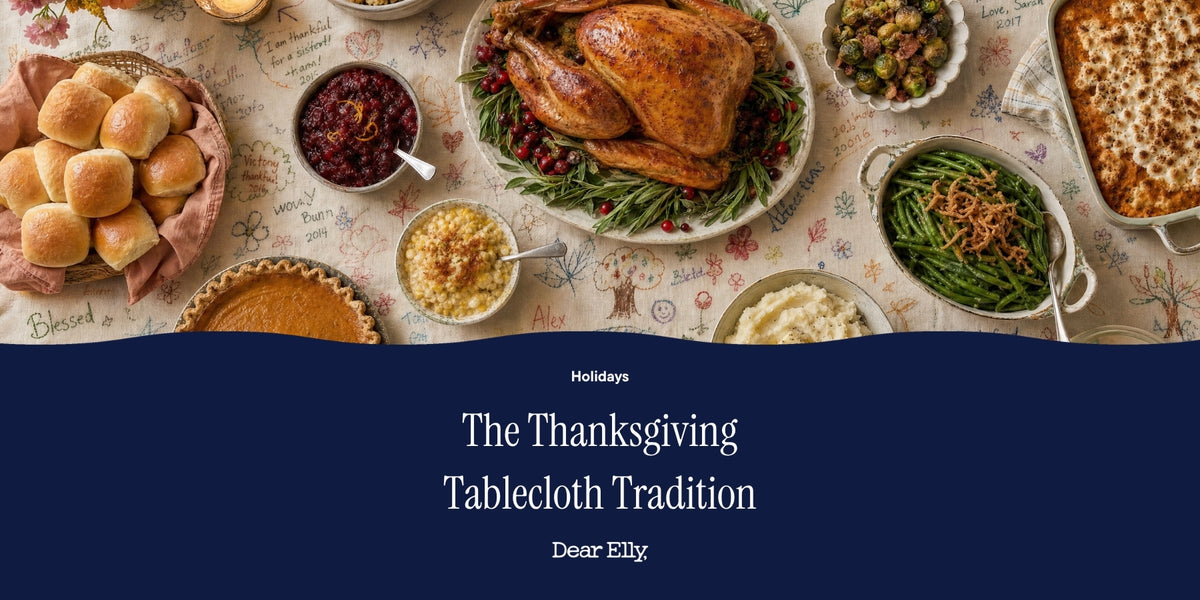 A Thanksgiving tablecloth scene with a roasted turkey, rolls, stuffing, green beans, mashed potatoes, cranberry sauce, and pumpkin pie, overlaid with a dark blue banner reading 'The Thanksgiving Tablecloth Tradition' and 'Dear Elvy'.